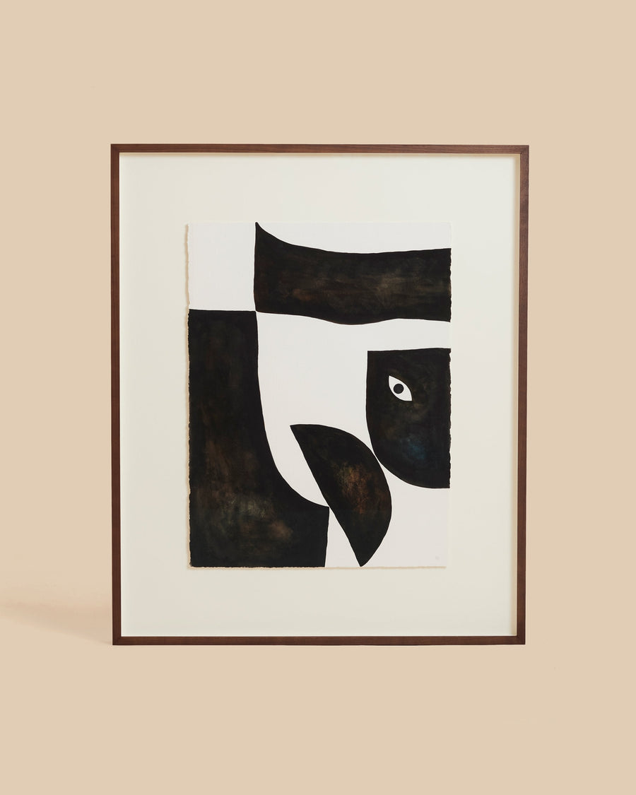 Framed collage by Hermentaire in a slim dark wood frame, black and deep brown shapes cut against white with one pale eye at the centre