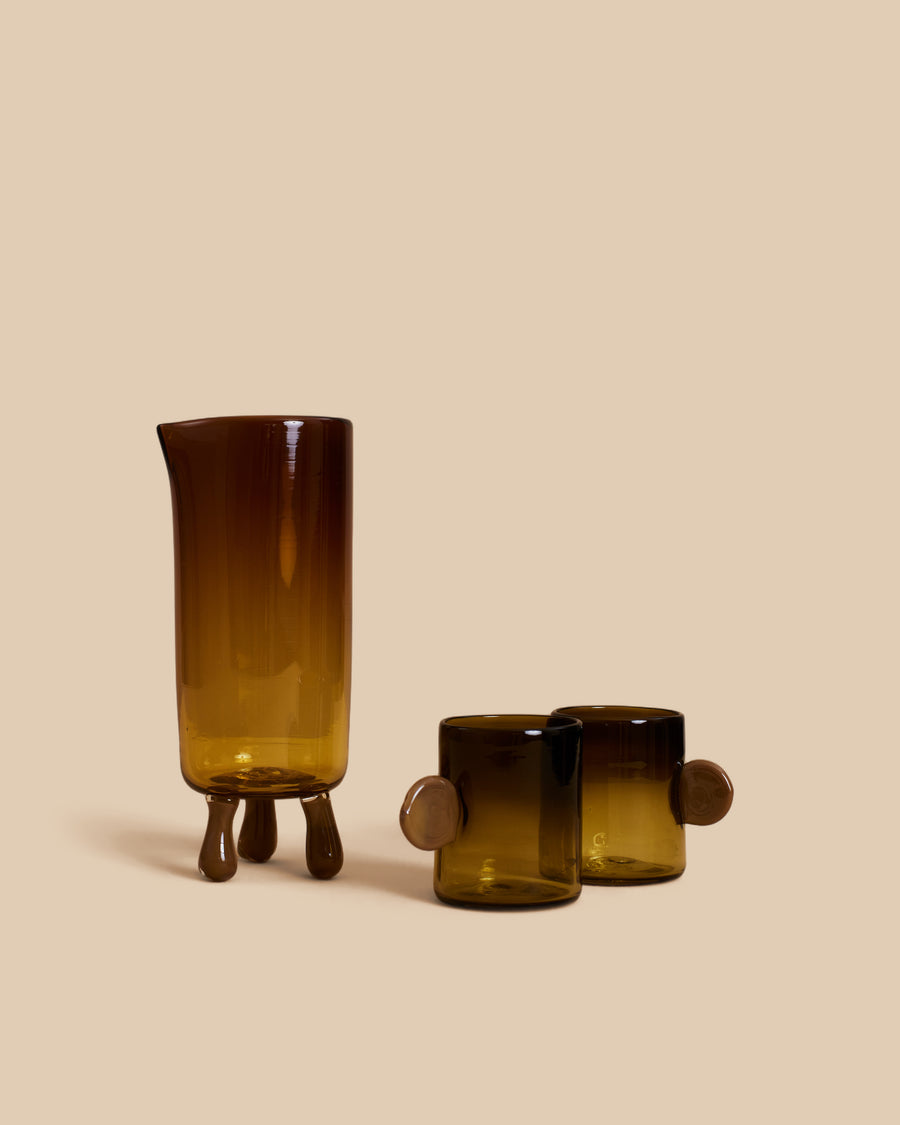Dash Carafe and Dot Cup Set by Sticky Glass in amber and tobacco, a hand-blown amber carafe on three glass feet with two olive cups with disc handles