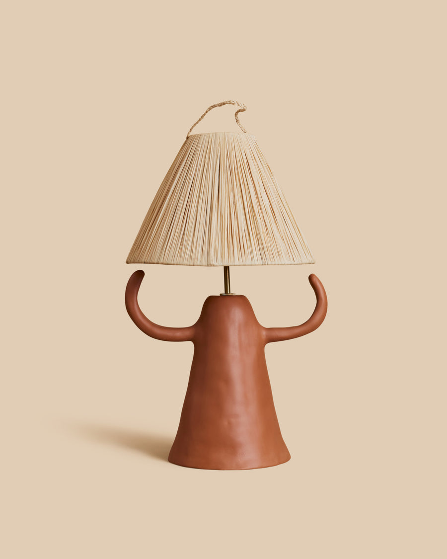Donna Lamp by Marta Bonilla, a terracotta table lamp with a cone-shaped base and two curved arms, under a pleated raffia shade