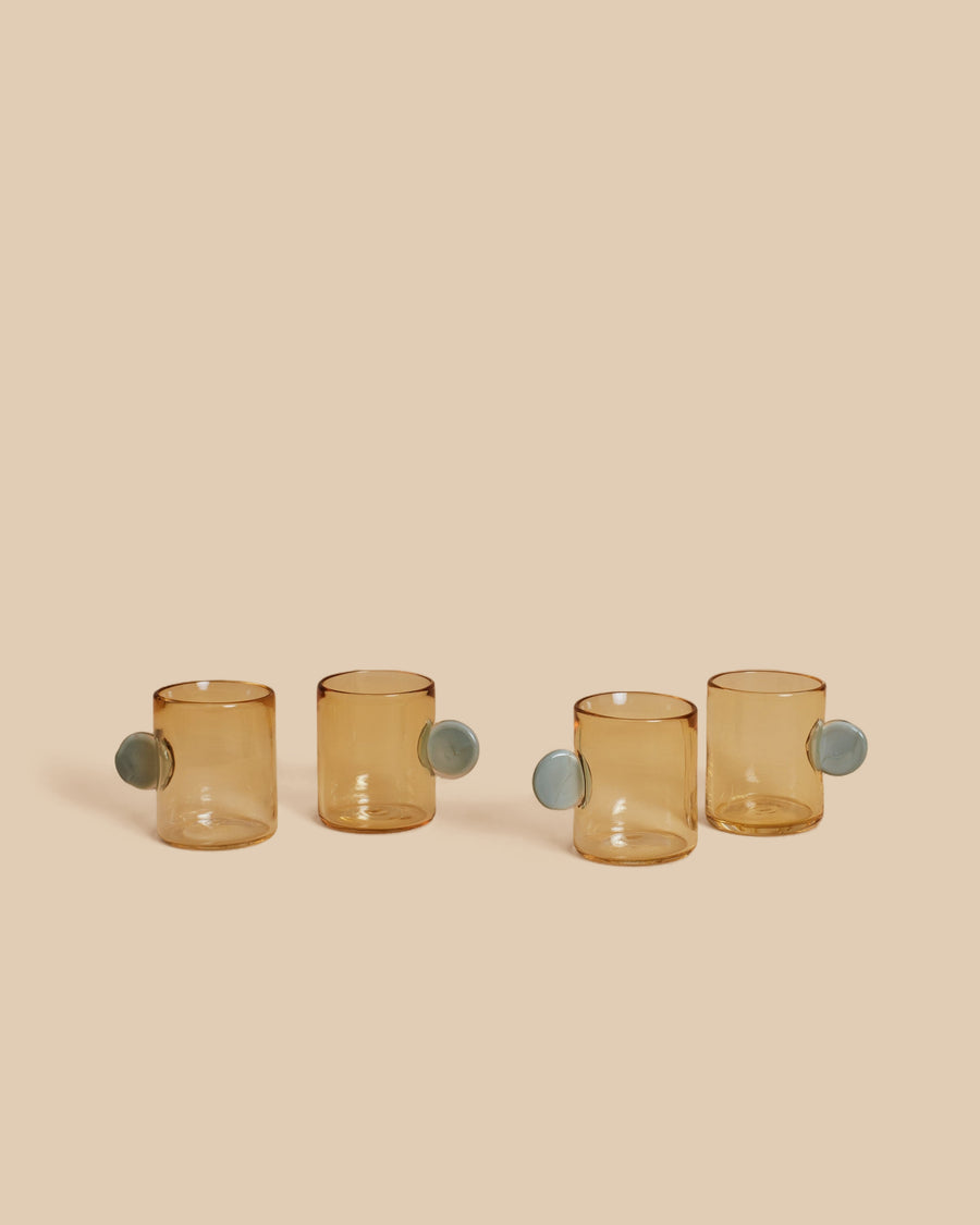 Dot Glass Set by Sticky Glass in whiskey and grey, four hand-blown pale amber cups with blue-grey disc handles