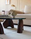 Orion coffee table with glass top and three hand-sculpted black walnut legs, crafted in Brooklyn, showcasing its unique shapes and sustainable design