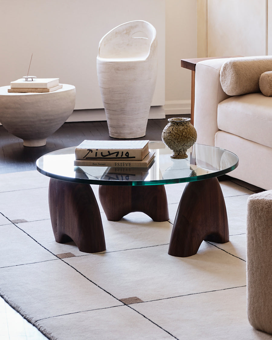 Orion coffee table with glass top and three hand-sculpted black walnut legs, crafted in Brooklyn, showcasing its unique shapes and sustainable design
