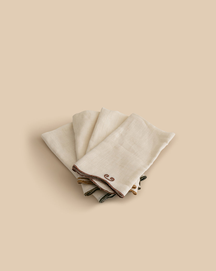 Set of four Twist Napkins by Sophie Lou Jacobsen, featuring natural linen with a wavy edge and contrasting embroidered details in terre, bordeaux, ocre, and olive.
