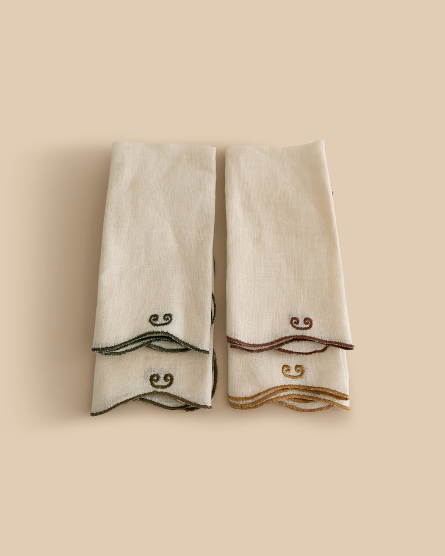 Set of four Twist Napkins by Sophie Lou Jacobsen, featuring natural linen with a wavy edge and contrasting embroidered details in terre, bordeaux, ocre, and olive.