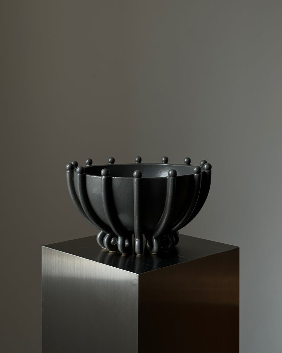 Hand-crafted ceramic bowl with Onyx finish, featuring sleek curves, vertical lines, and spherical accents by Devin Wilde.