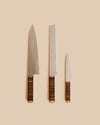 three premium handmade chef's knives with hardwood and brass handles, including a bread, paring, and gyuto knife