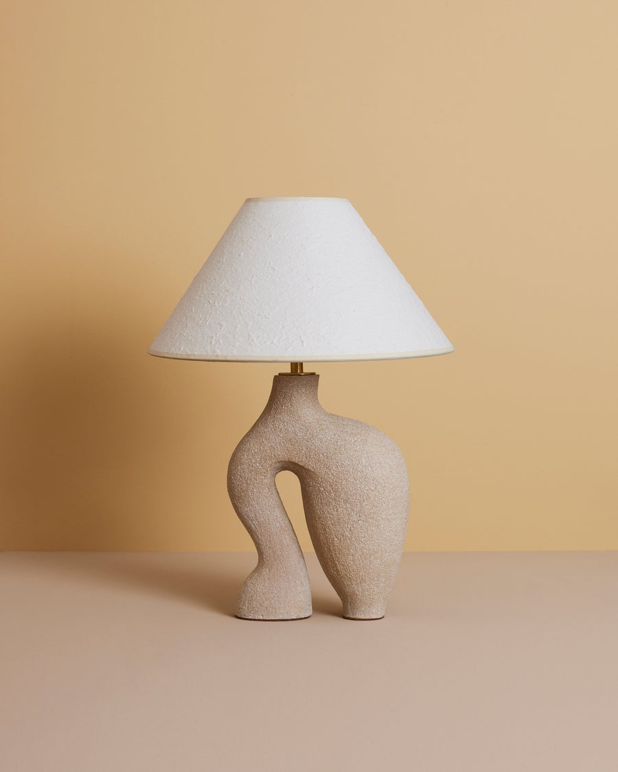 stylized image of sand-colored abstract sculptural ceramic table lamp with ivory rice paper shade