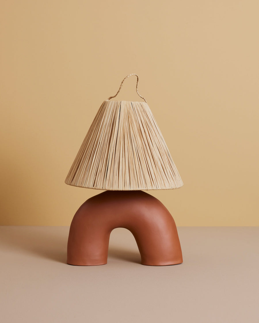 handmade terracotta rustic clay table lamp in a half circle-shaped base with a straw shade