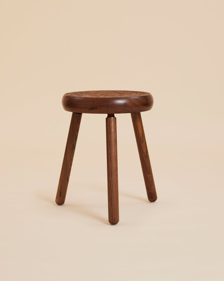 stylized image of elegant minimalist handcrafted solid walnut wood stool with carved textured seat