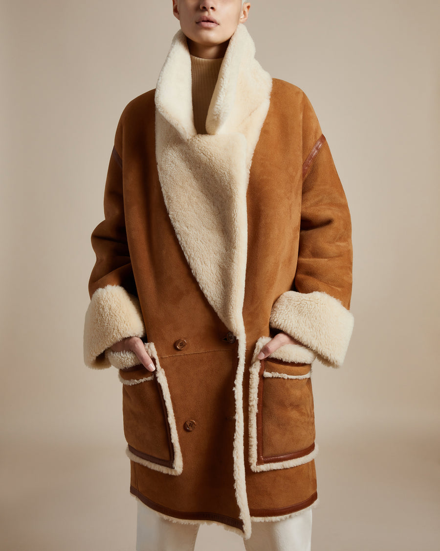 knee-length reversible shearling coat with camel-colored suede, double breasted body, dropped shoulders and generous fold up cuffs on body